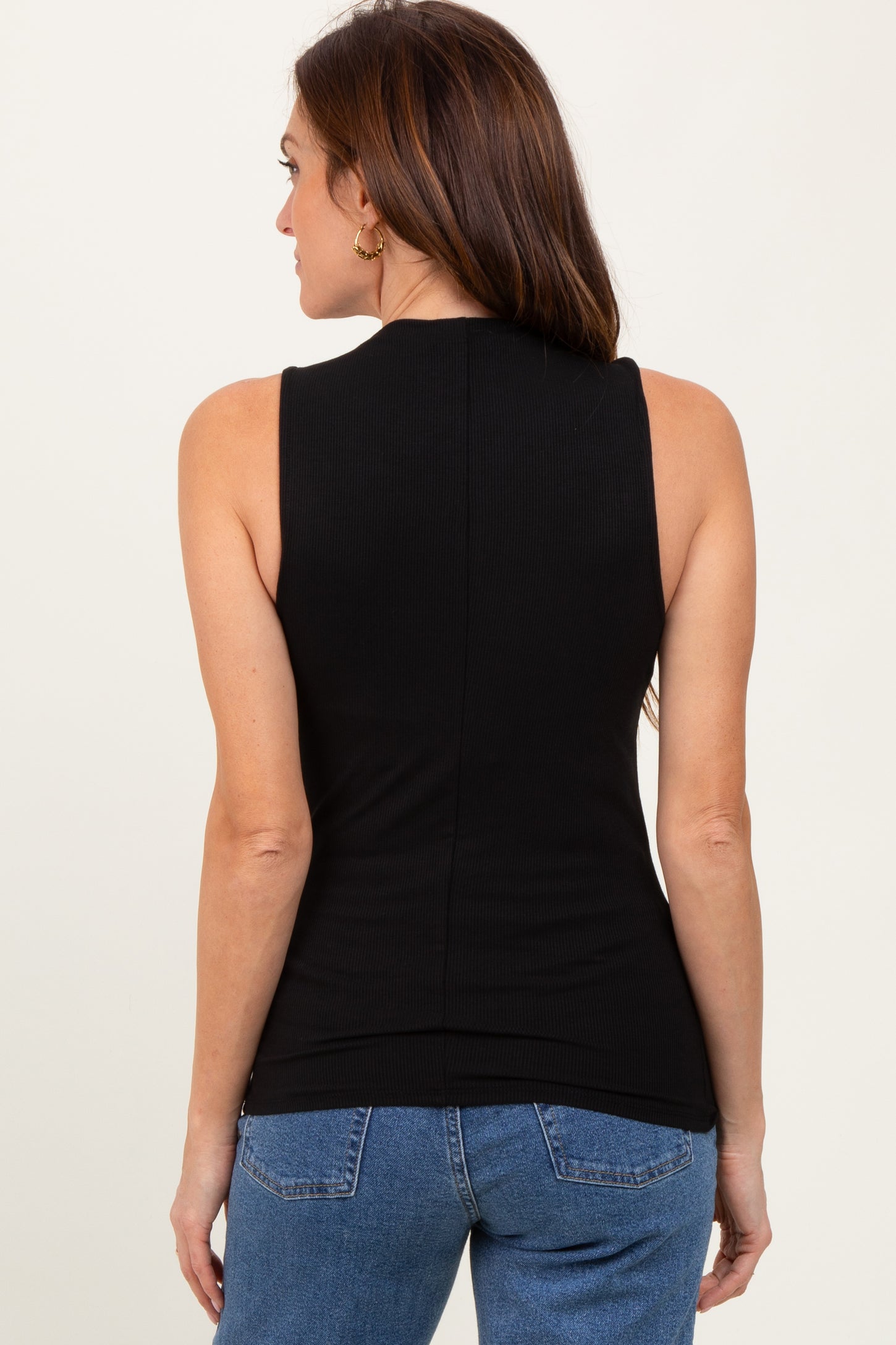 woman wearing a sleeveless black ribbed top with a high neckline, viewed from the back with blue jeans