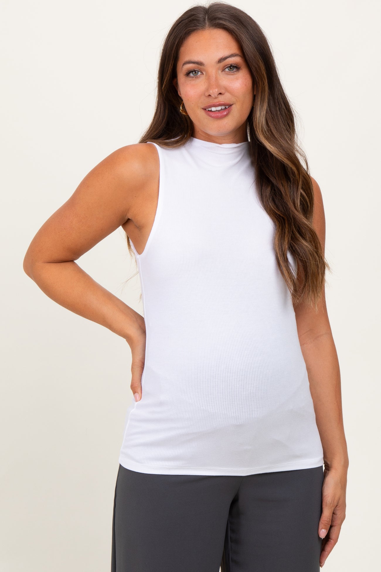 woman wearing a white sleeveless maternity top with a mock neck and fitted style, showcasing her baby bump