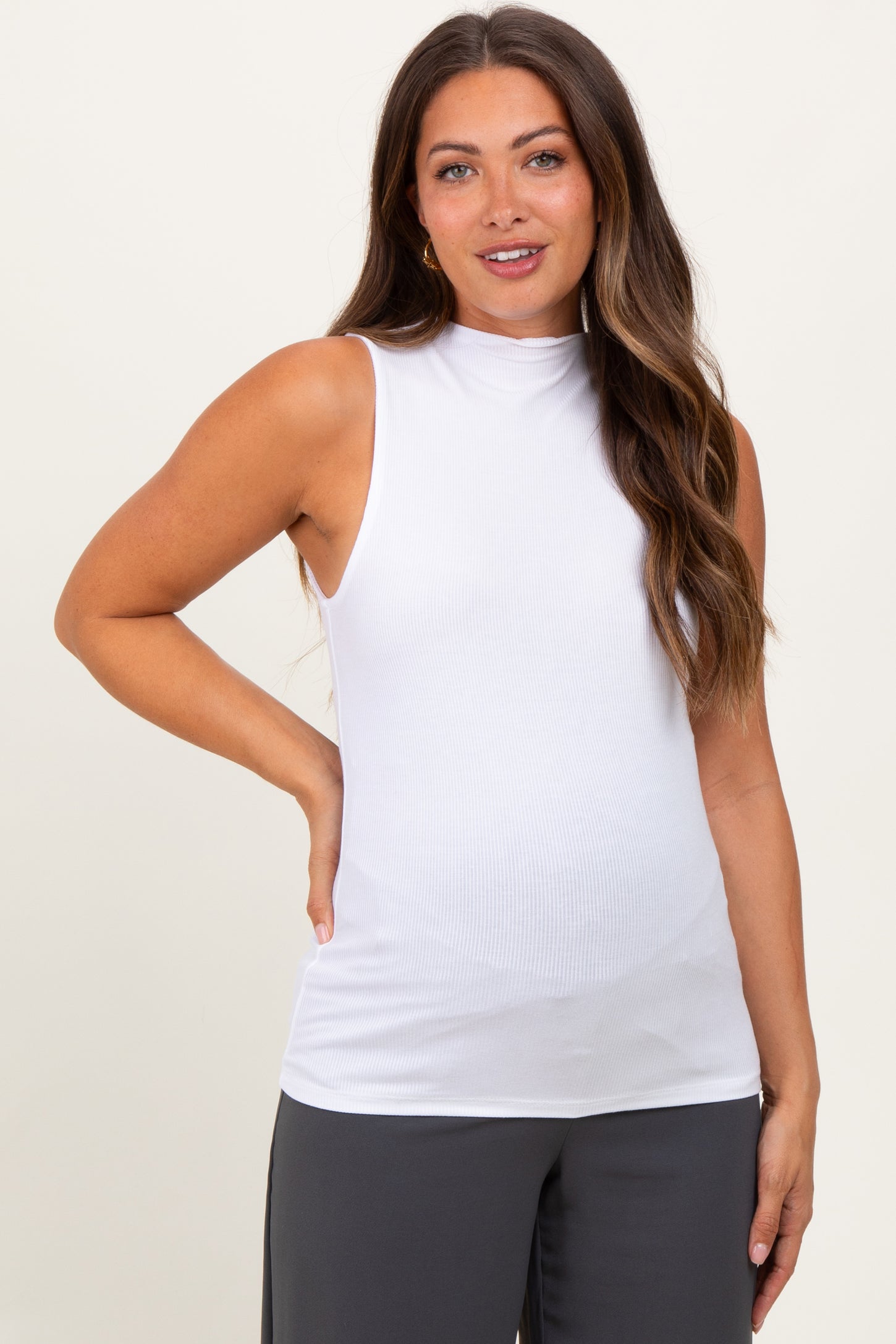 woman wearing a white sleeveless maternity top with a mock neck and fitted style, showcasing her baby bump