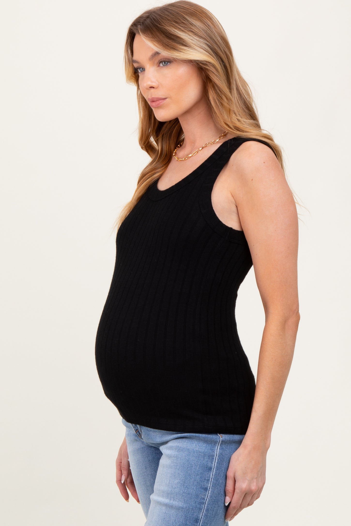 woman wearing a black ribbed maternity tank top and showing her baby bump, paired with light blue jeans