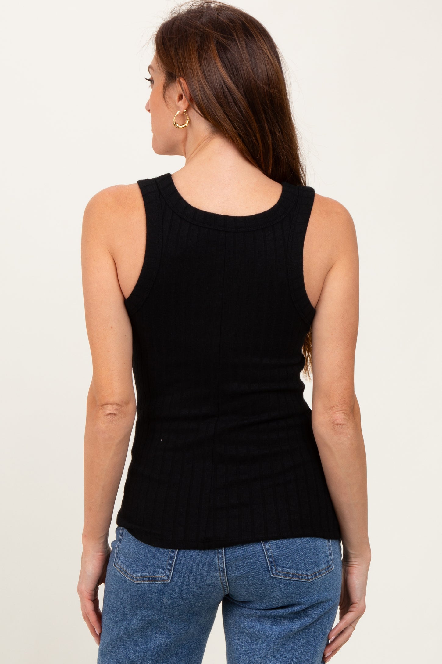 woman wearing a black ribbed tank top with a fitted silhouette and paired with blue jeans, viewed from the back