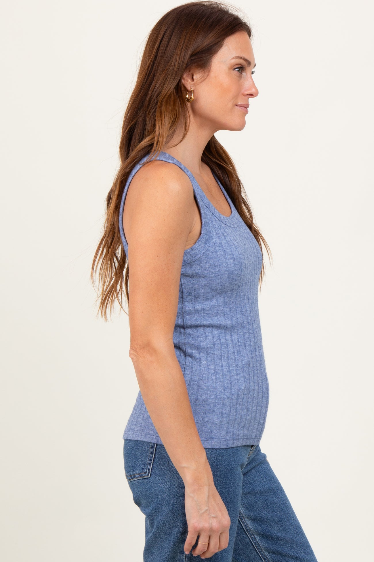 woman wearing a light blue ribbed tank top and jeans, viewed from the side