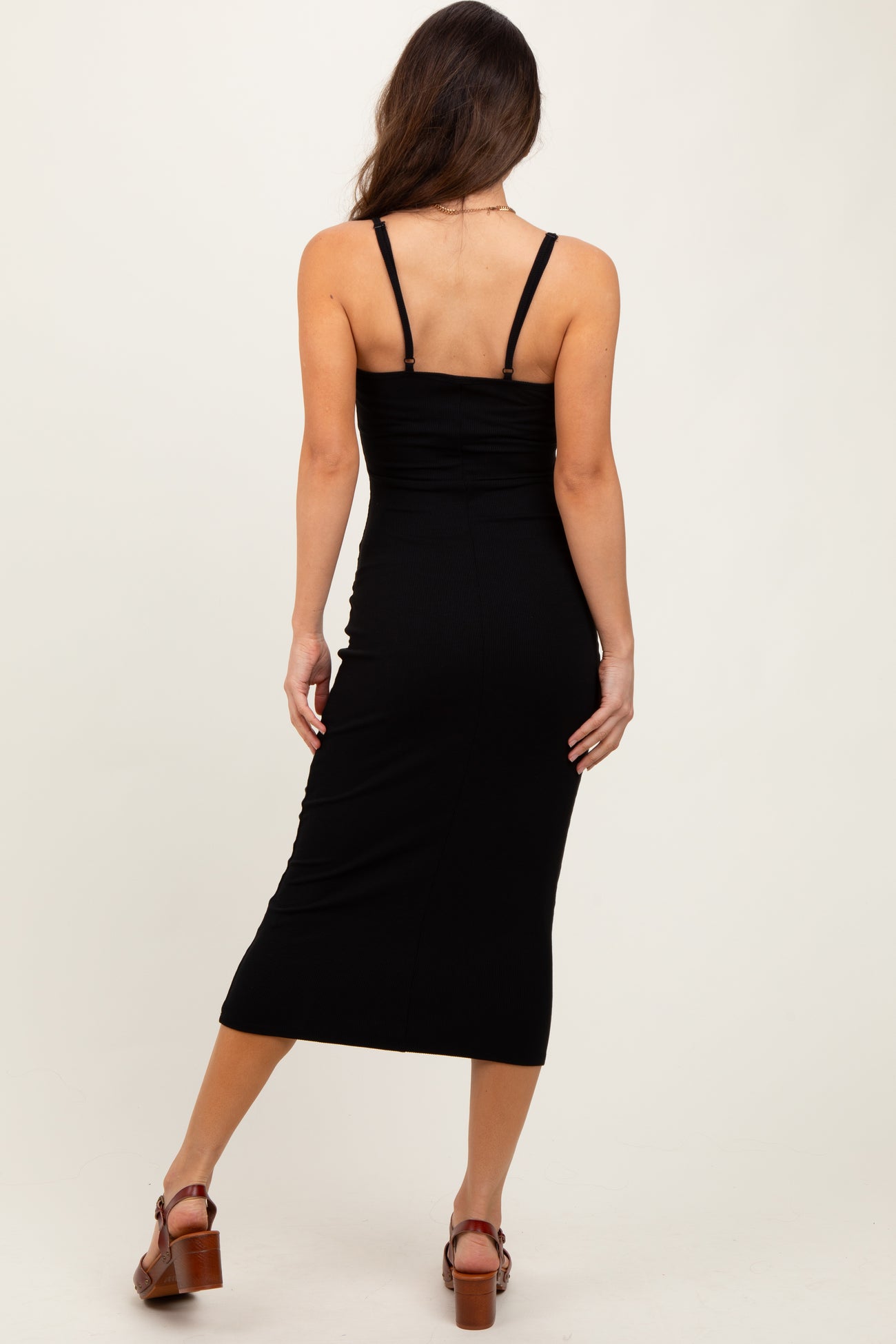 woman wearing a black ribbed midi dress with spaghetti straps, showing the back view and a fitted silhouette