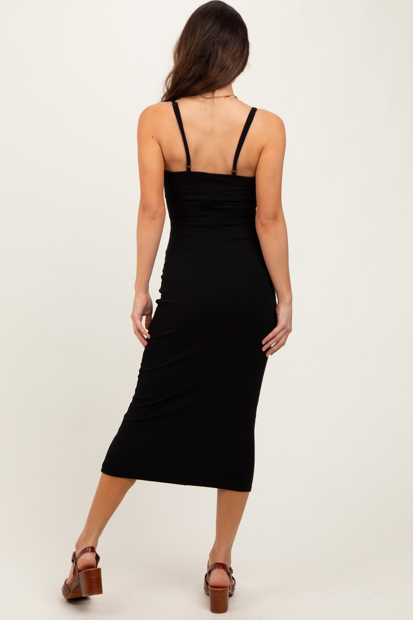 woman wearing a black ribbed midi dress with spaghetti straps, showing the back view and a fitted silhouette
