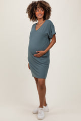 woman wearing a teal maternity dress with a v-neckline and short sleeves, holding her baby bump
