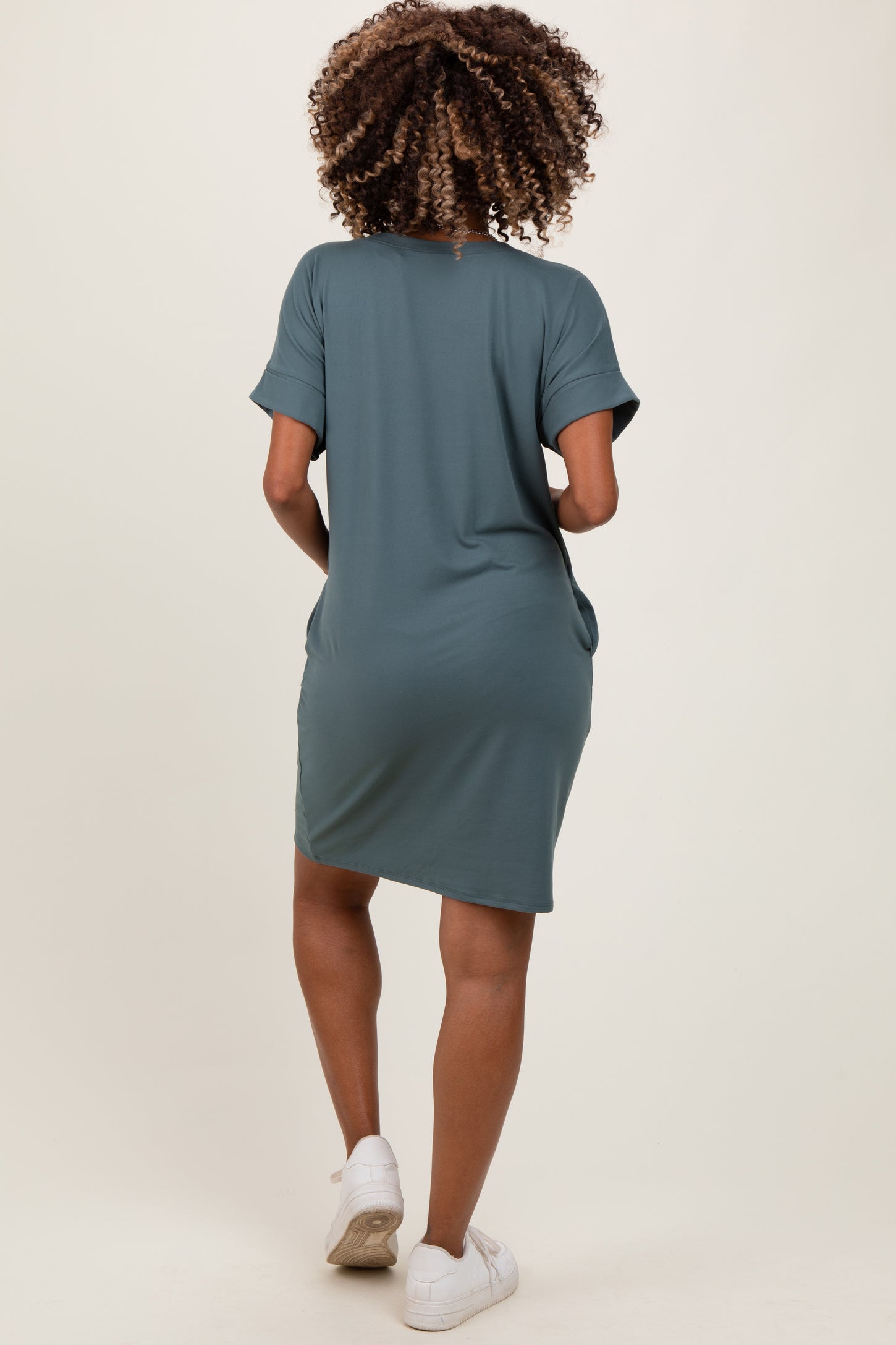 woman wearing a slate green short sleeve maternity dress with side pockets, styled casually with white sneakers