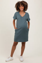 woman wearing a dark green short sleeve maternity dress with pockets and a baby bump visible