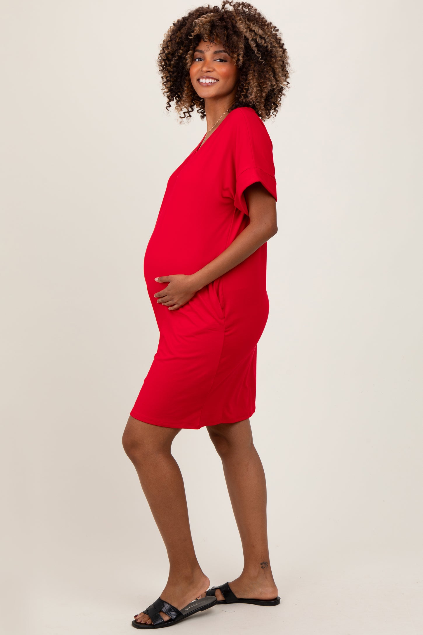 woman wearing a red short sleeve maternity dress, smiling and holding her baby bump