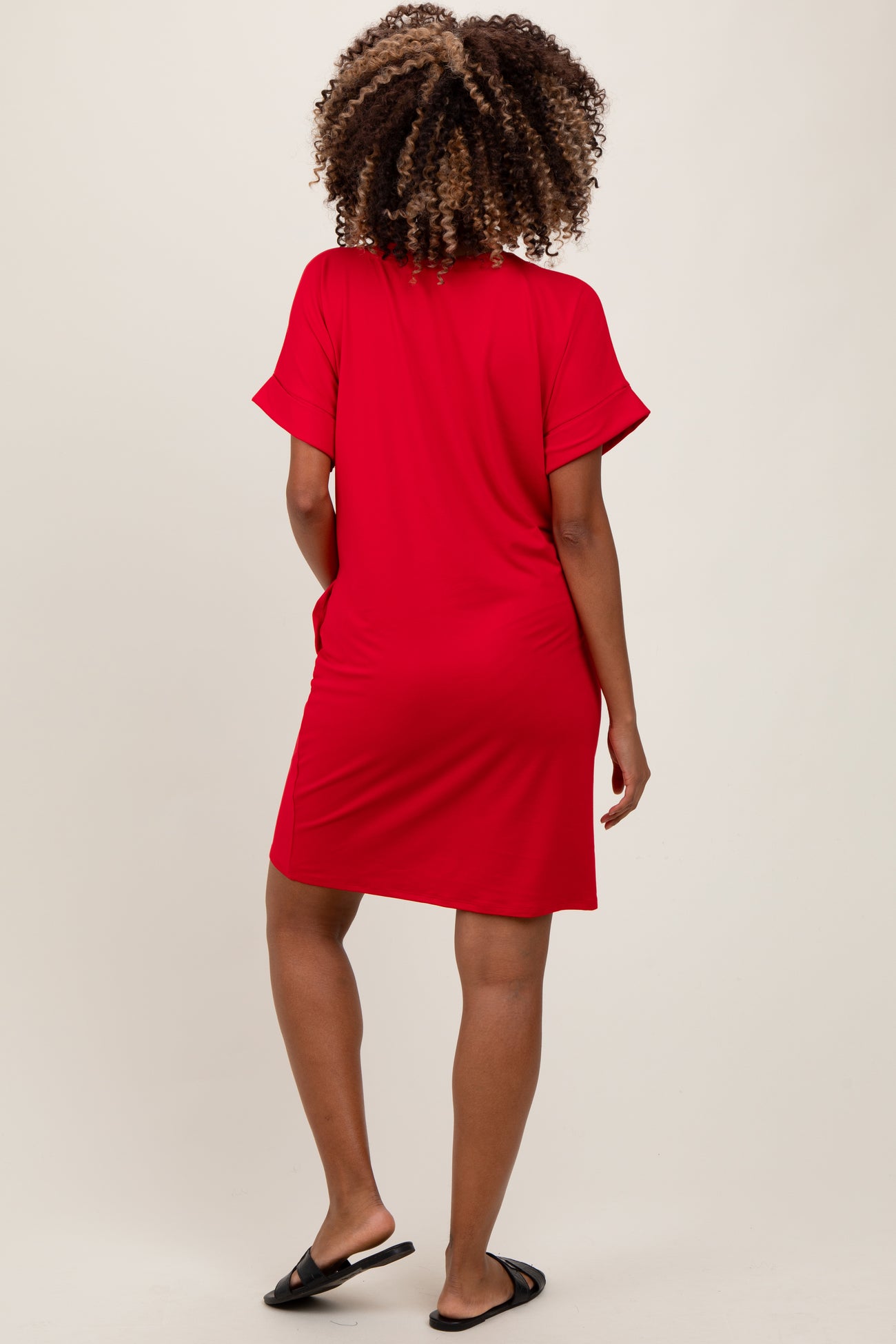 woman wearing a bright red maternity short sleeve dress, seen from the back, with a relaxed fit and pockets