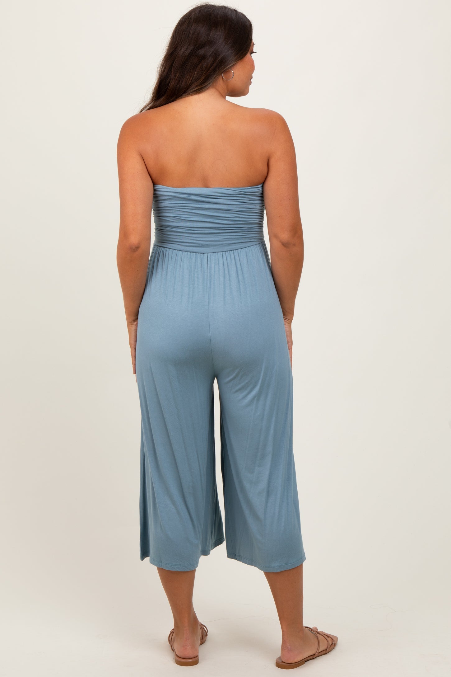 woman wearing a light blue strapless maternity jumpsuit with a smocked bodice and cropped legs, showing no baby bump