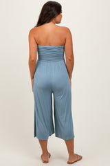 woman wearing a light blue strapless maternity jumpsuit with a smocked bodice and cropped legs, showing no baby bump