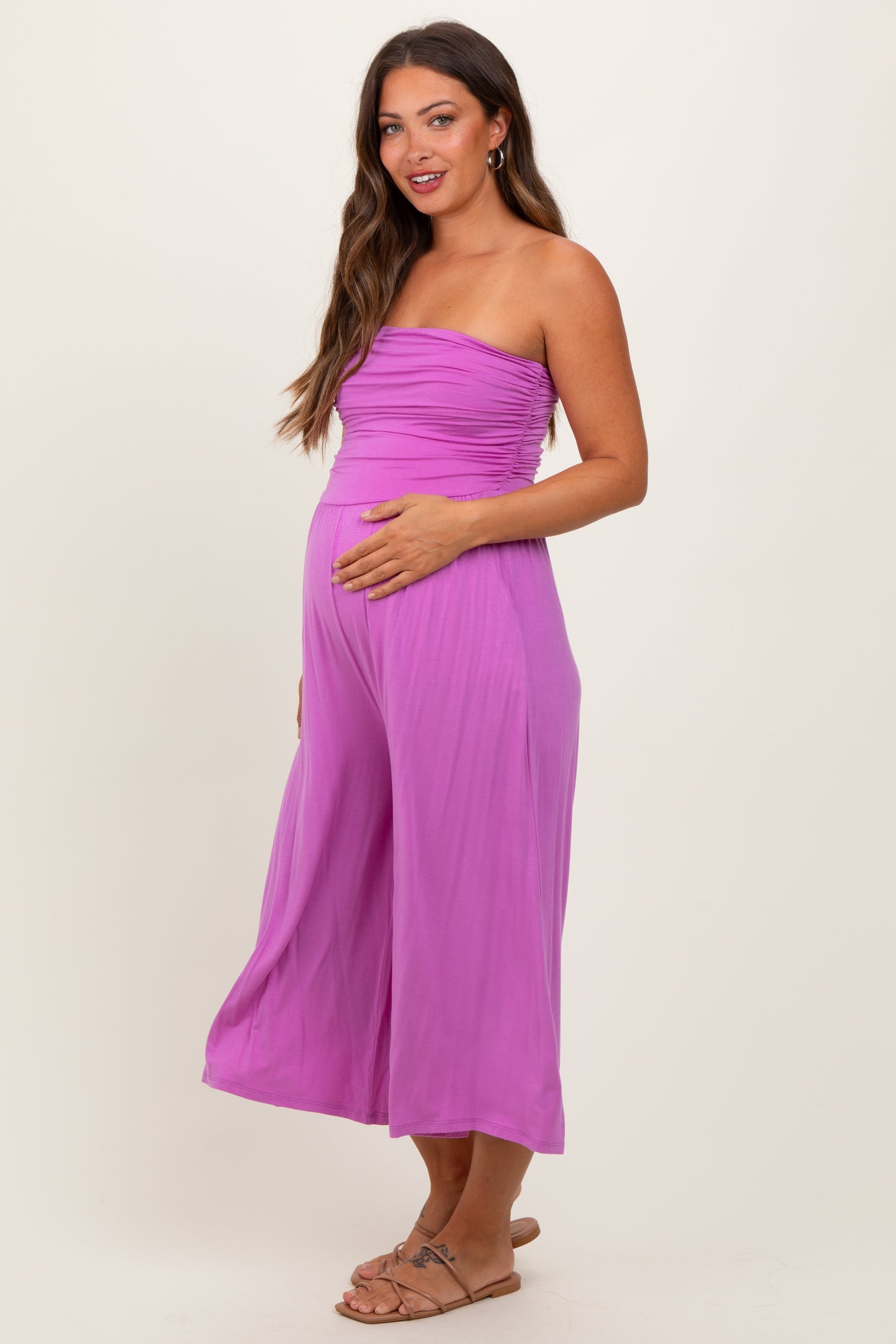 woman wearing a bright pink strapless maternity jumpsuit and holding her baby bump