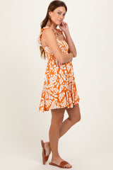 woman wearing an orange floral print mini dress with a tie shoulder detail and posing sideways