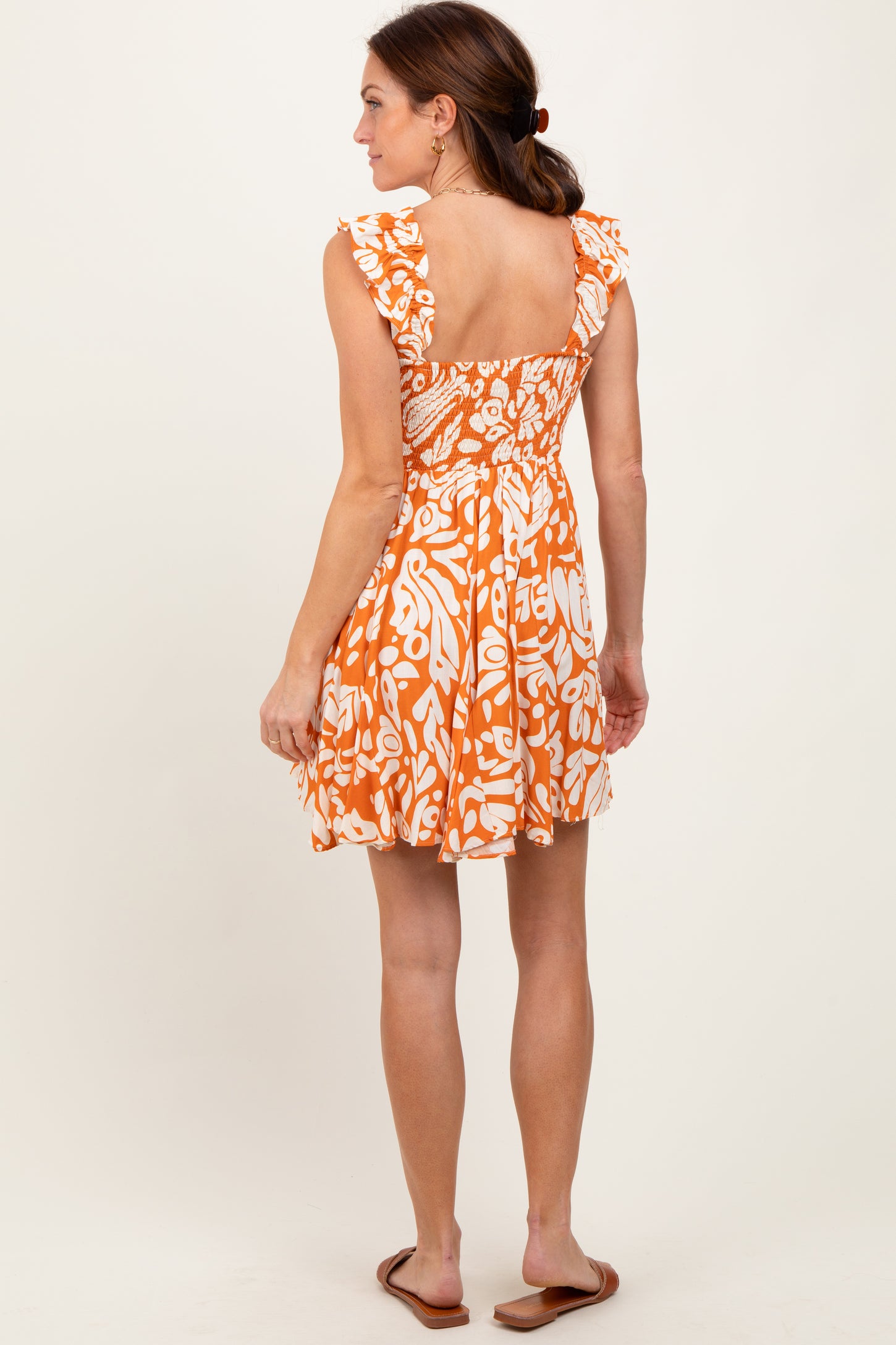 woman wearing an orange and white patterned sundress with ruffled sleeves and a smocked back