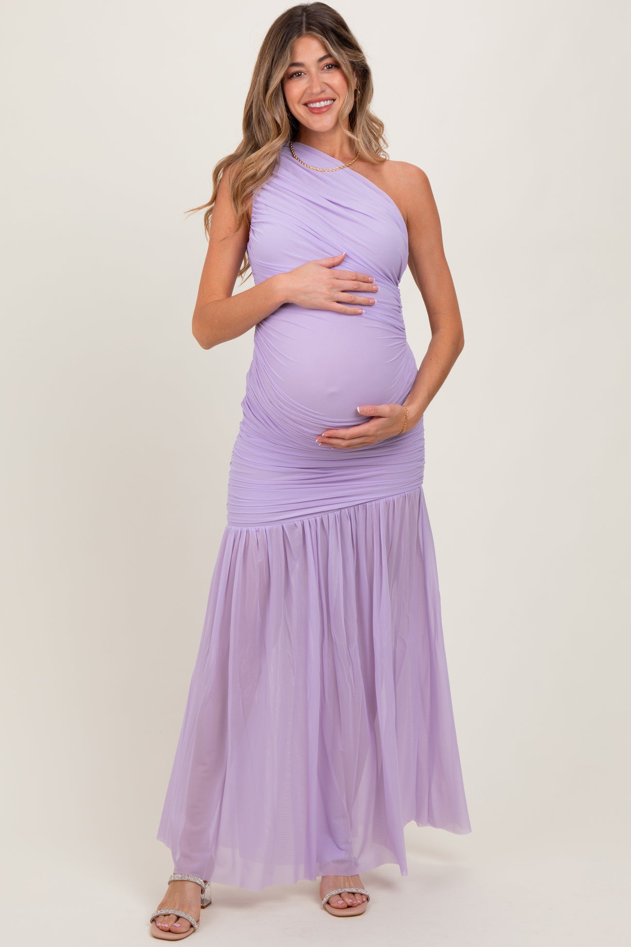 woman wearing a purple one-shoulder maternity gown with a flowing skirt and holding her baby bump