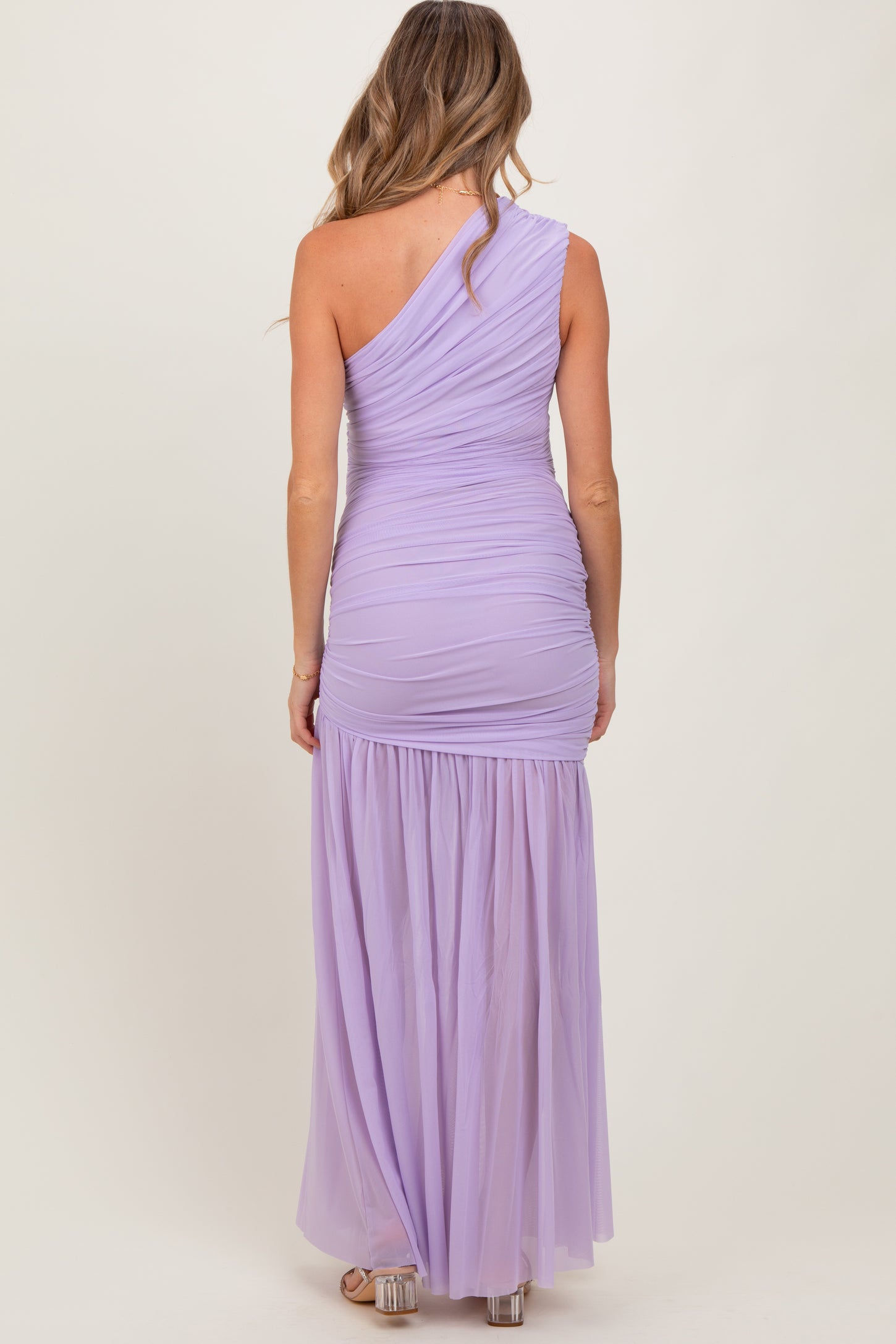 woman wearing a lilac one-shoulder maternity gown with ruched detailing and a flowing skirt
