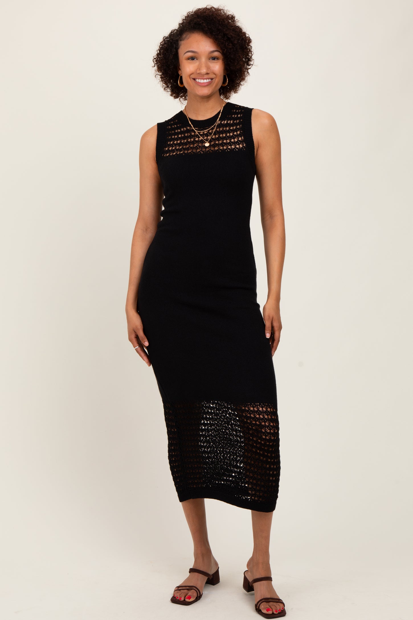 woman wearing a black sleeveless knit midi dress with open weave detailing and strappy sandals