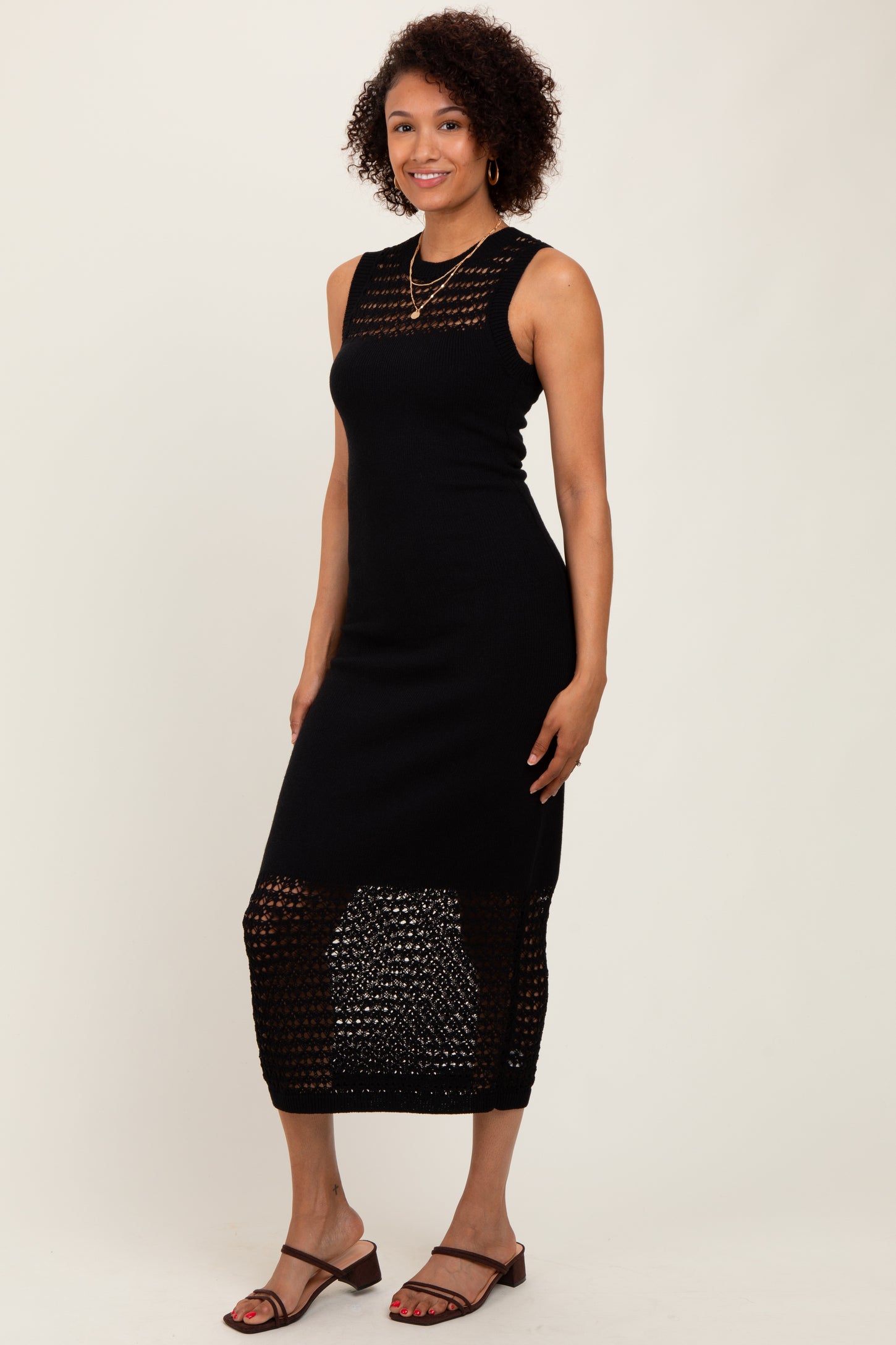 woman wearing a black sleeveless knit midi dress with a lace pattern and side slits, paired with brown sandals