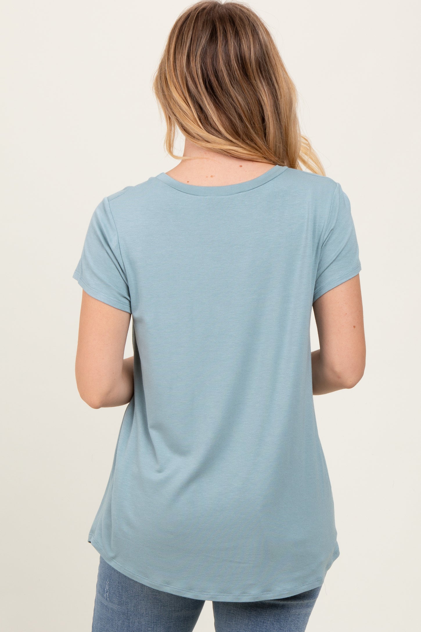 woman wearing a light blue short sleeve top, viewed from the back, with a rounded hem and relaxed fit