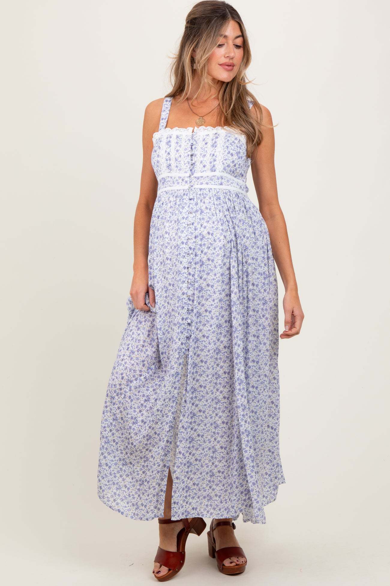 woman wearing a floral print maternity maxi dress with adjustable straps and a flowing skirt, showcasing her baby bump