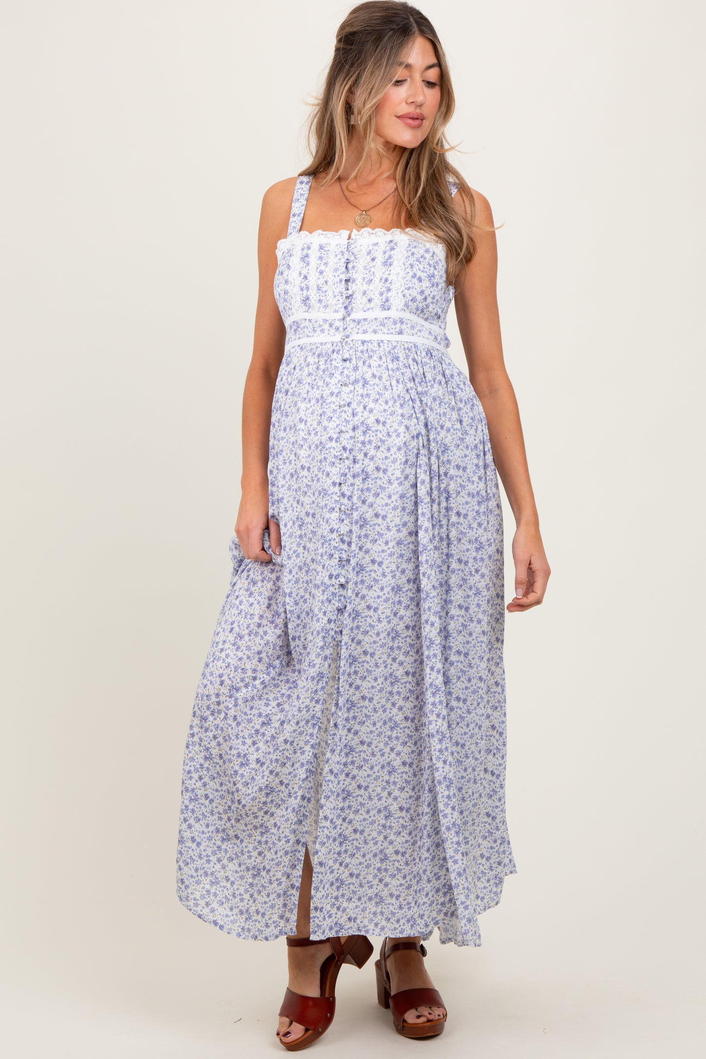 woman wearing a floral print maternity maxi dress with adjustable straps and a flowing skirt, showcasing her baby bump