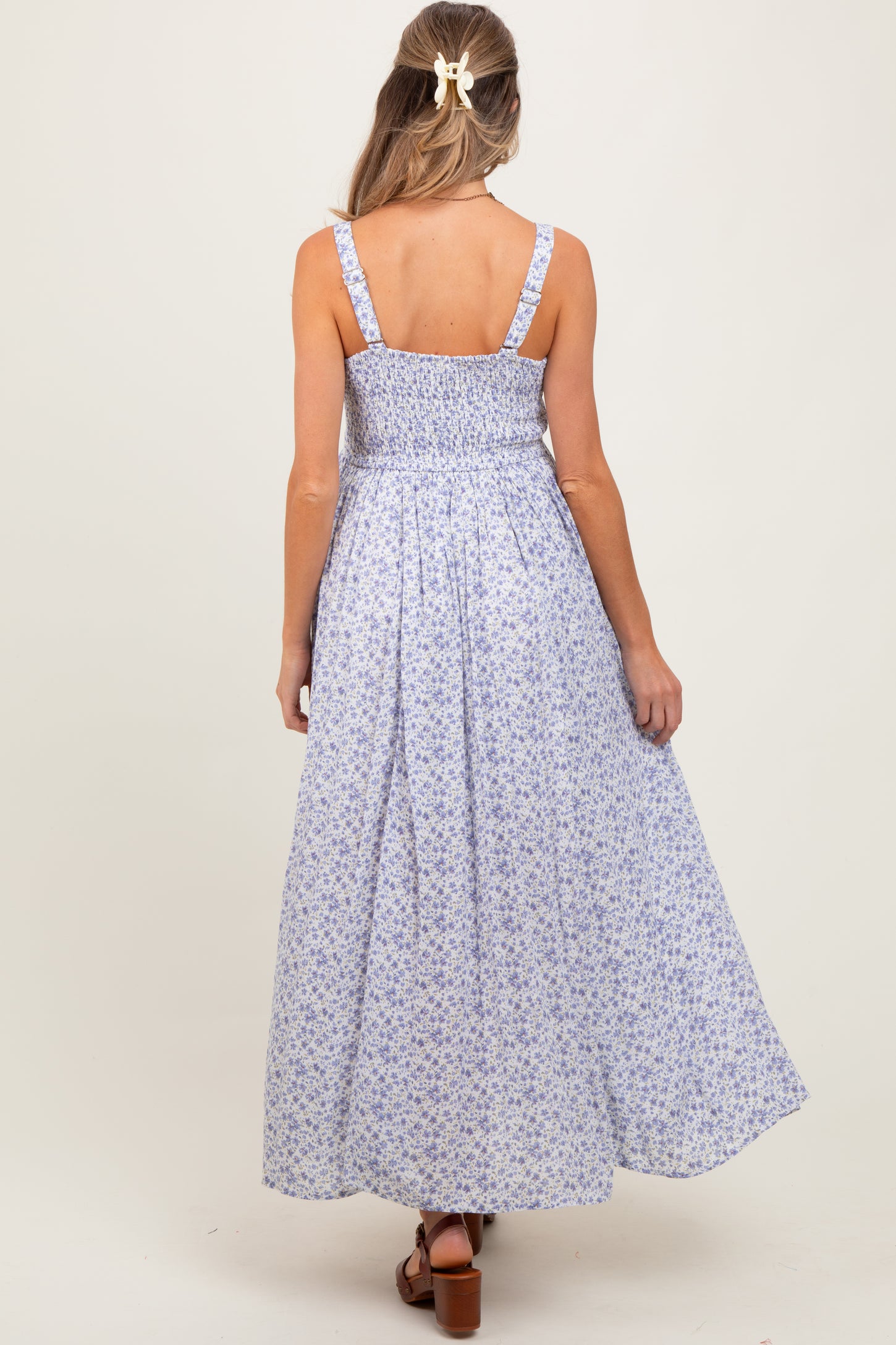woman wearing a blue floral print maternity maxi dress, showing a smocked back detail and a flowing skirt