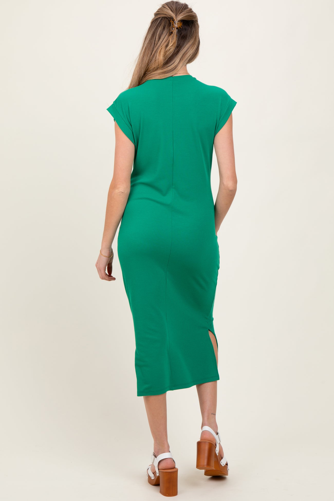 woman wearing a green cap sleeve maternity dress with a side slit, showing her baby bump from the back