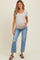 woman wearing a light gray short sleeve maternity top and distressed blue maternity jeans, cradling her baby bump