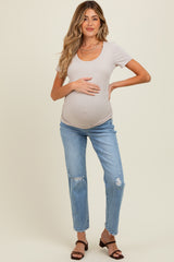 woman wearing a light gray short sleeve maternity top and distressed blue jeans, holding her baby bump