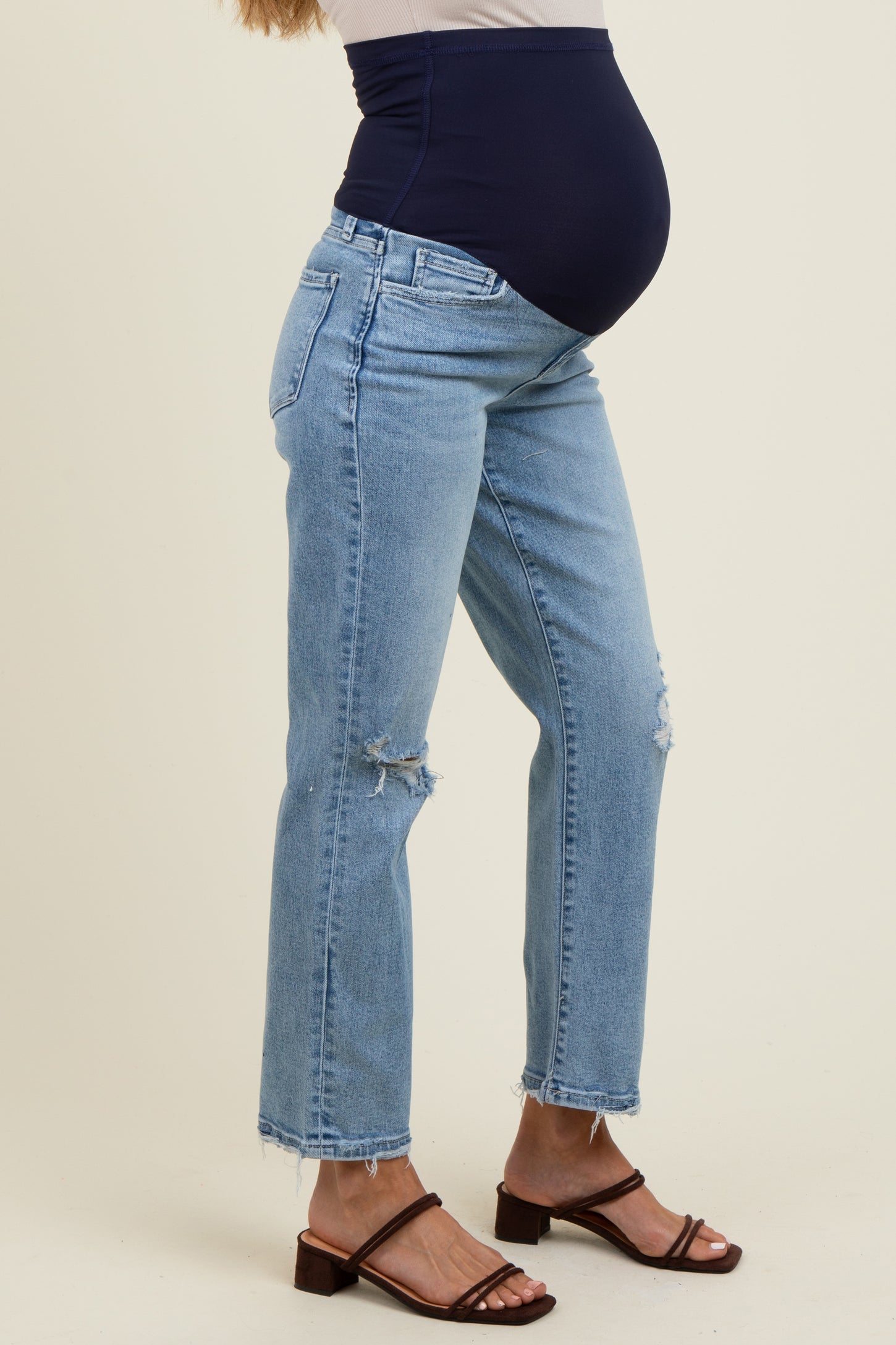 woman wearing light blue distressed maternity jeans with a navy blue over-the-bump panel and a visible baby bump