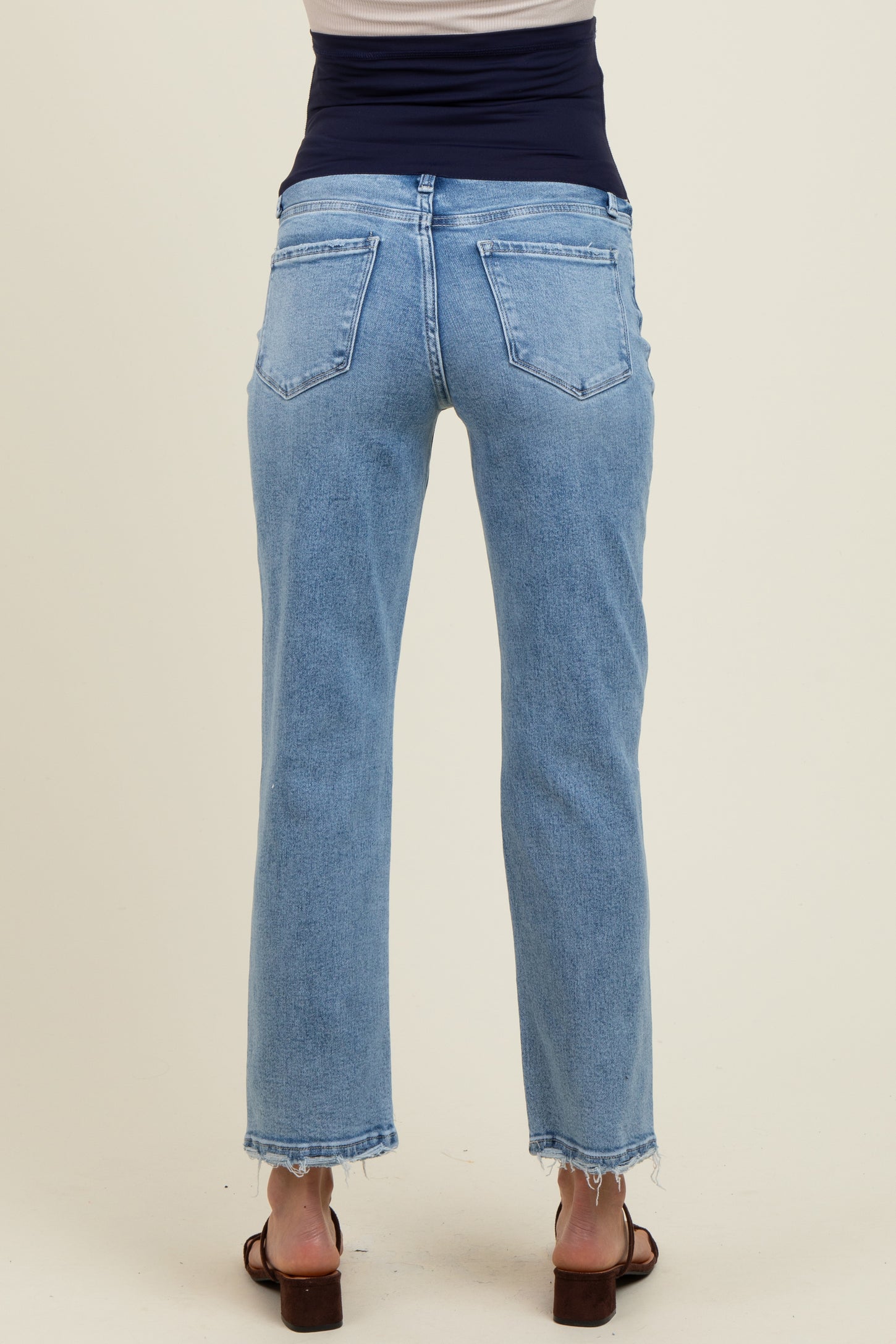 woman wearing light blue maternity jeans with a frayed hem, showing a comfortable fit at the back