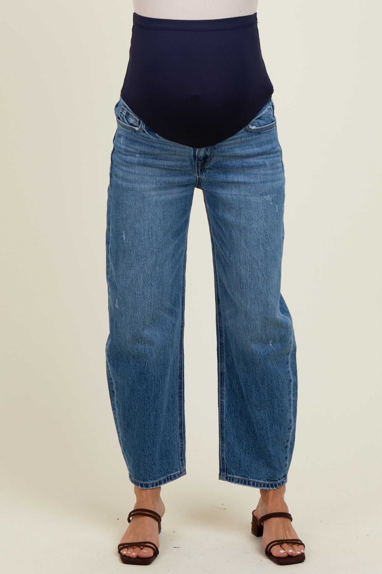 woman wearing dark blue maternity jeans with a stretchy waistband and a relaxed fit, styled with brown heeled sandals