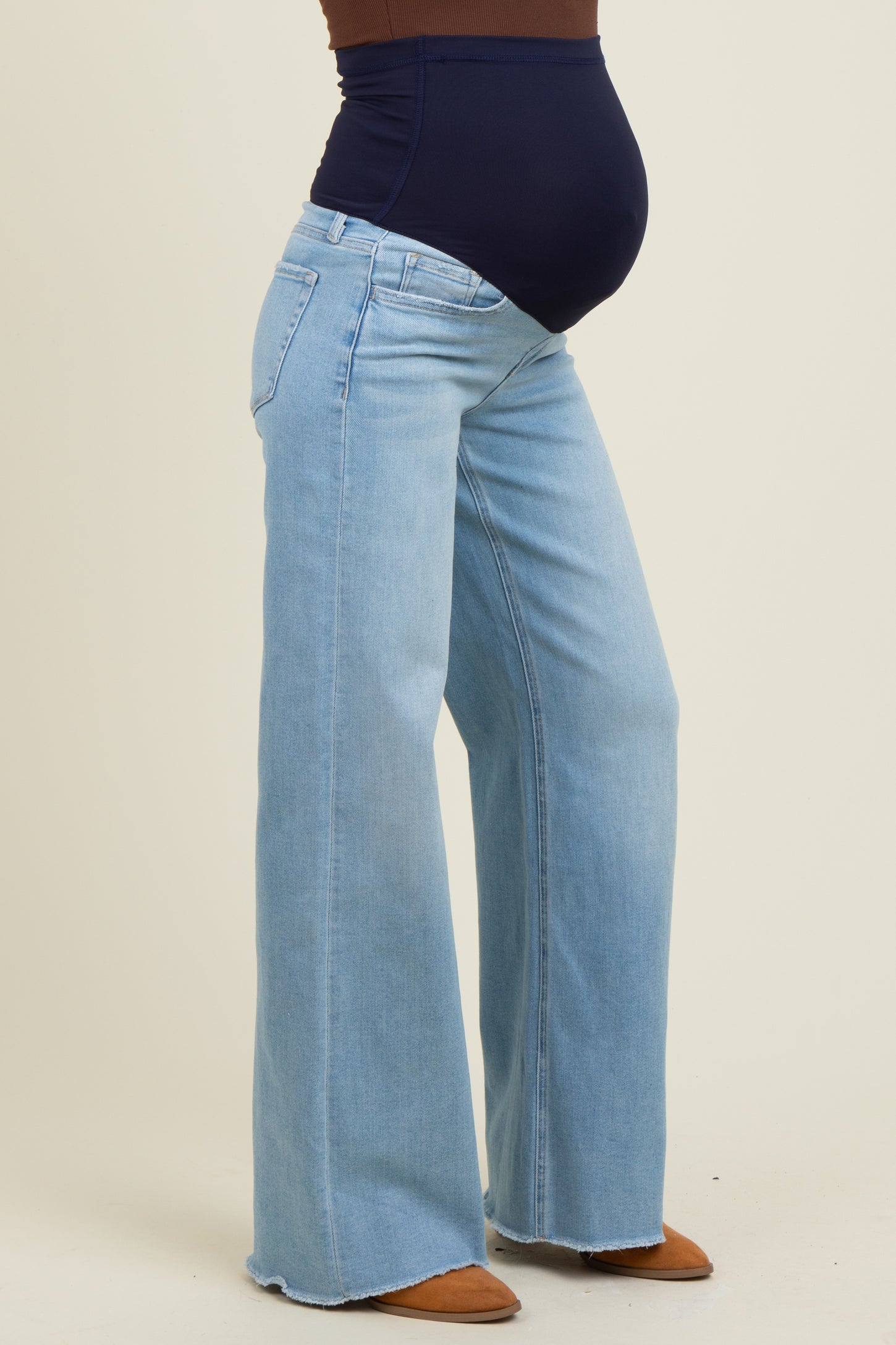woman wearing light blue maternity jeans with a high waist and flared legs, showcasing a visible baby bump