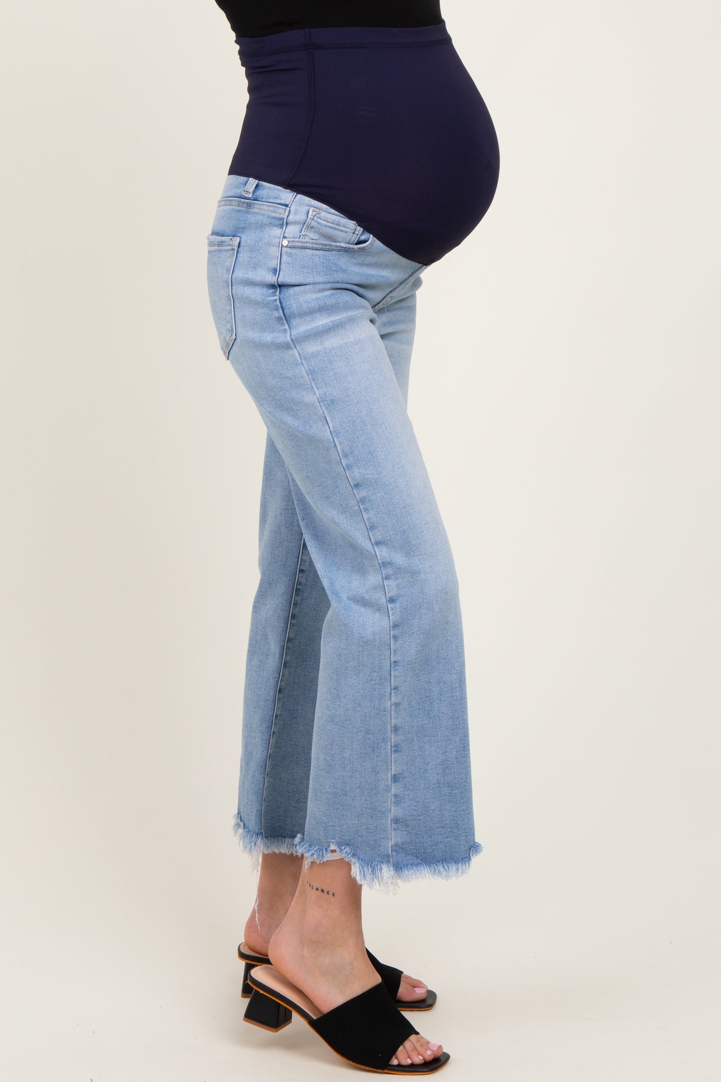 woman wearing light blue maternity jeans with a frayed hem and a dark blue belly band, showcasing her baby bump