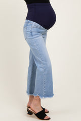 woman wearing light blue maternity jeans with a frayed hem and a dark blue belly band, showcasing her baby bump