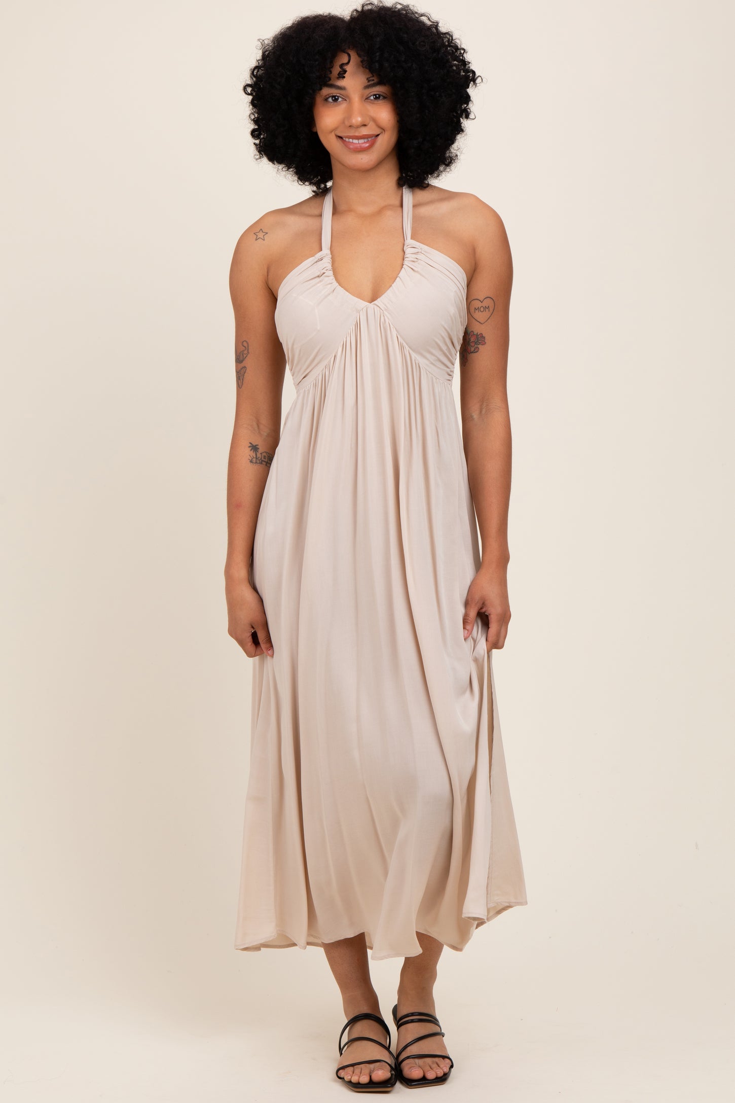 woman wearing a beige halter neck maxi dress with gathered detailing and slim straps