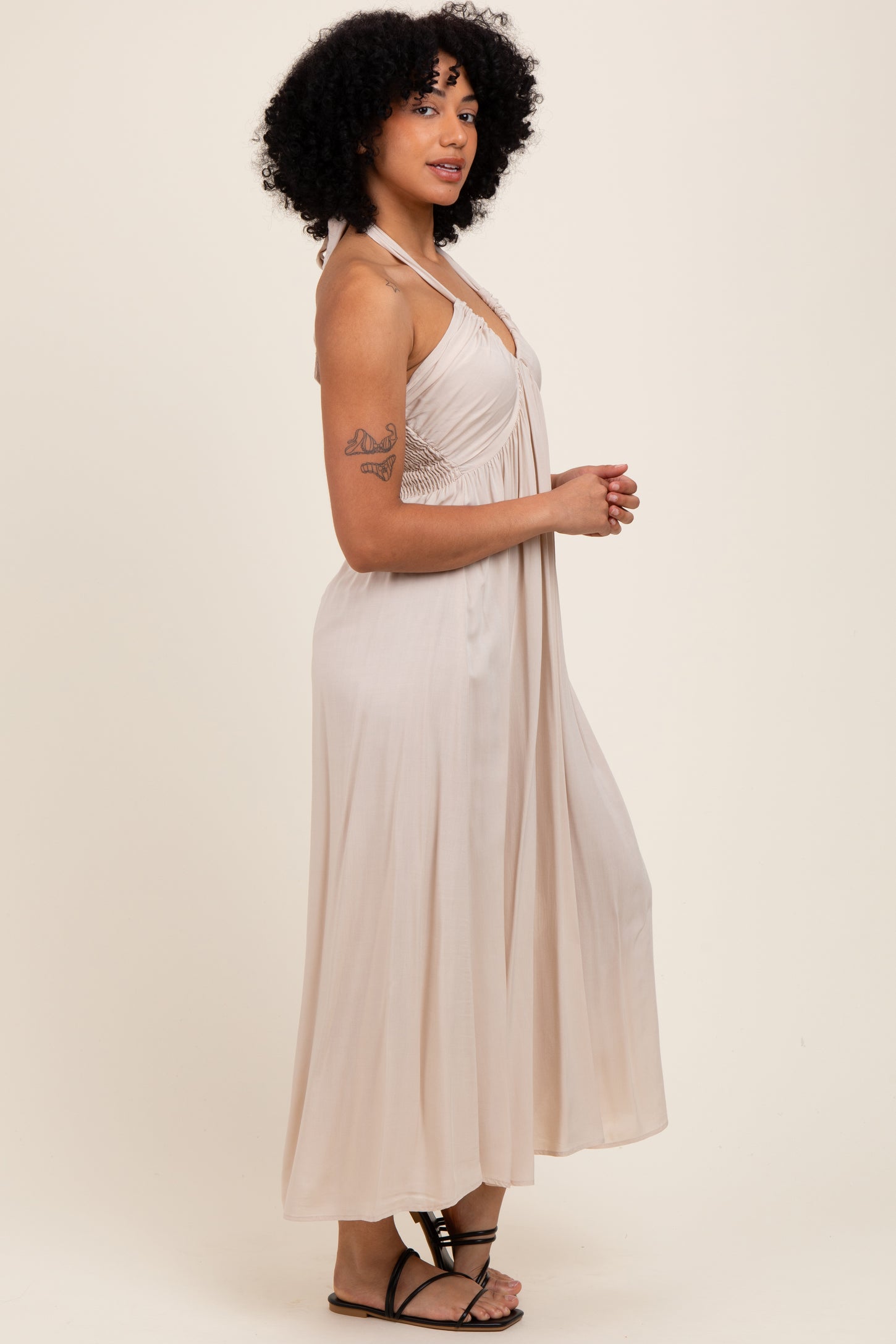 woman wearing a beige halter neck maxi dress with a flowy silhouette and a fitted bodice