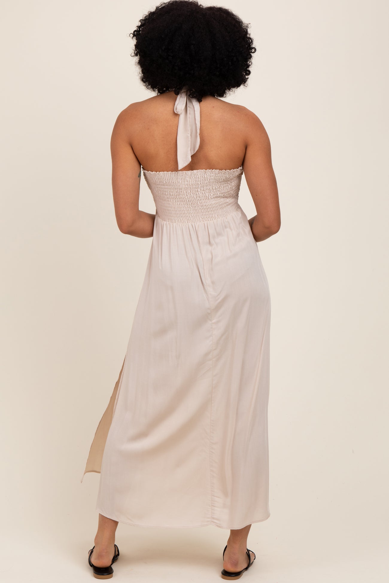 woman wearing a backless cream maxi dress with a smocked bodice and side slit
