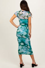 woman wearing a form-fitting teal floral midi dress with a sheer overlay and short sleeves, viewed from the back