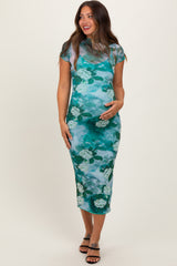 woman wearing a green floral print maternity dress and cradling her baby bump