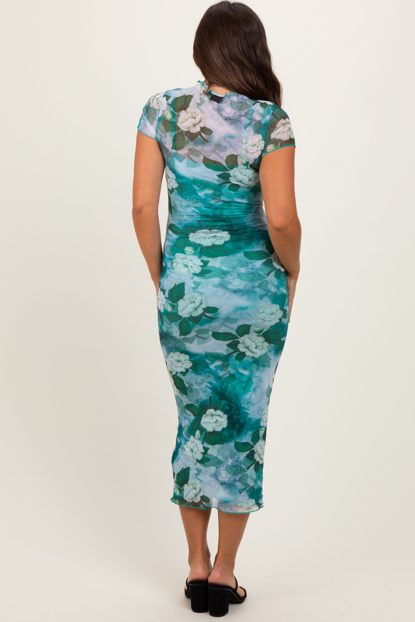 woman wearing a floral print maternity midi dress in shades of teal and green, with short sleeves and a fitted silhouette