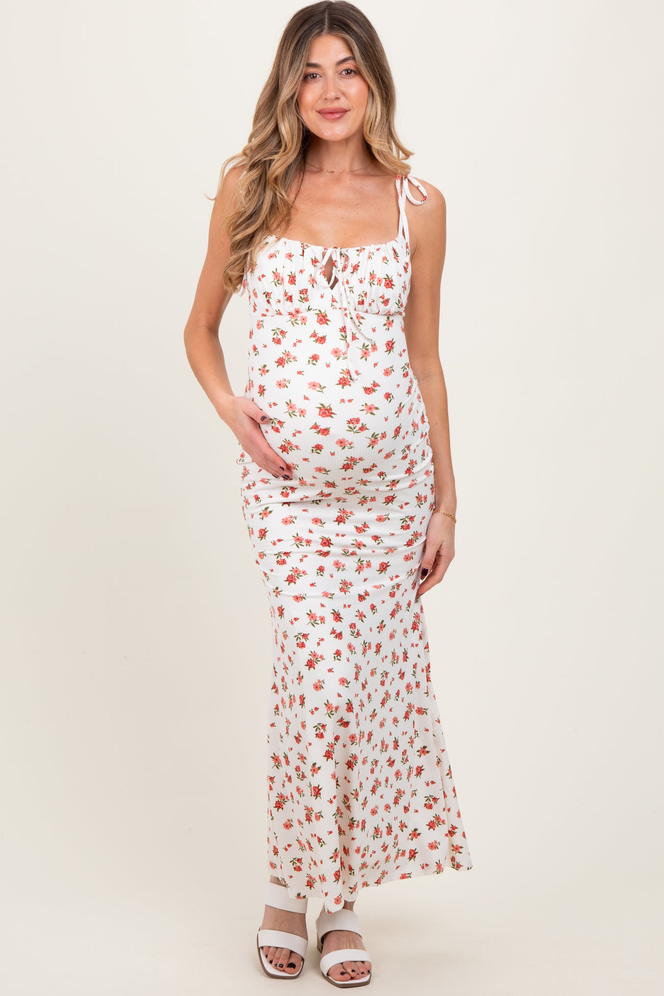 woman wearing a white floral maternity maxi dress and holding her baby bump