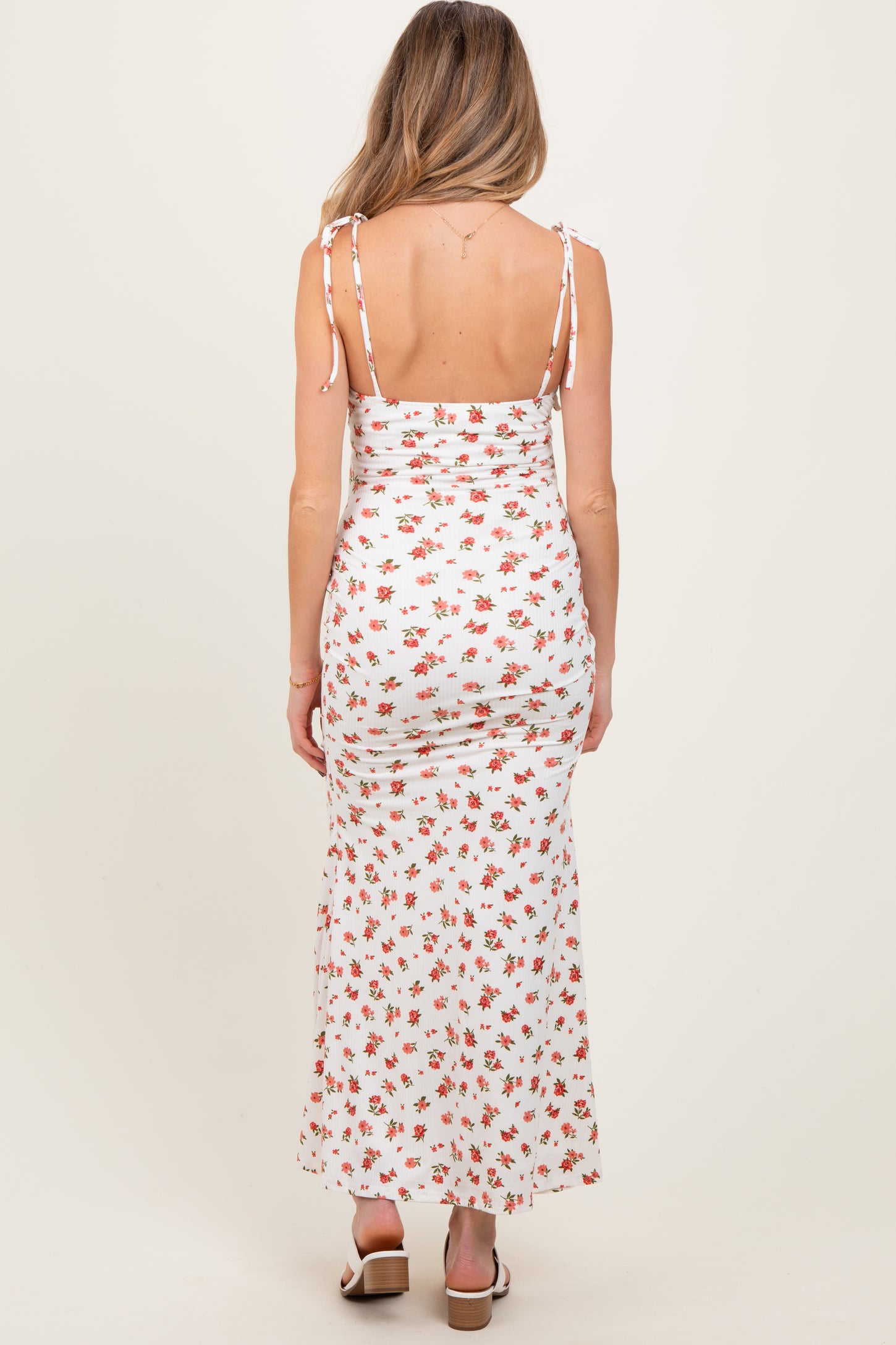 woman wearing a white floral maternity maxi dress with adjustable shoulder ties, showcasing a fitted silhouette