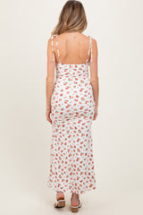 woman wearing a white floral maternity maxi dress with adjustable shoulder ties, showcasing a fitted silhouette