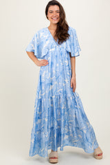 woman wearing a light blue floral maxi dress with flutter sleeves and a tiered skirt