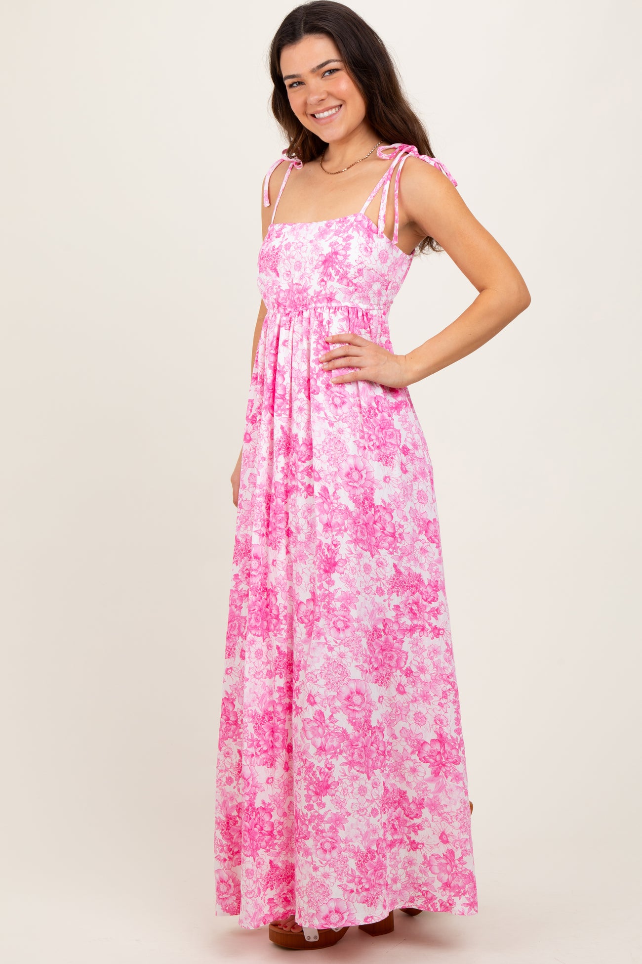 woman wearing a pink floral maxi dress with tie shoulder straps and a flowy silhouette