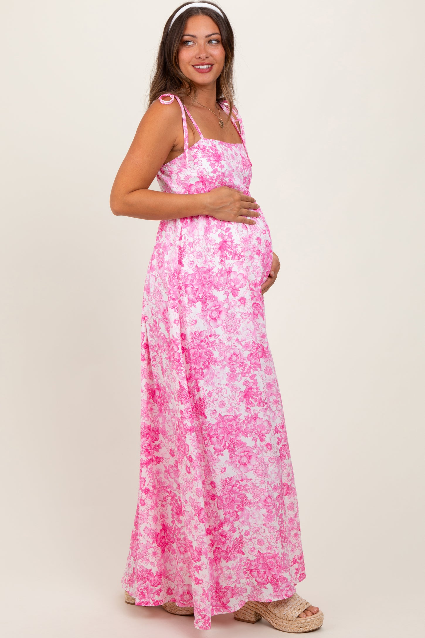 woman wearing a pink floral maxi maternity dress and holding her baby bump