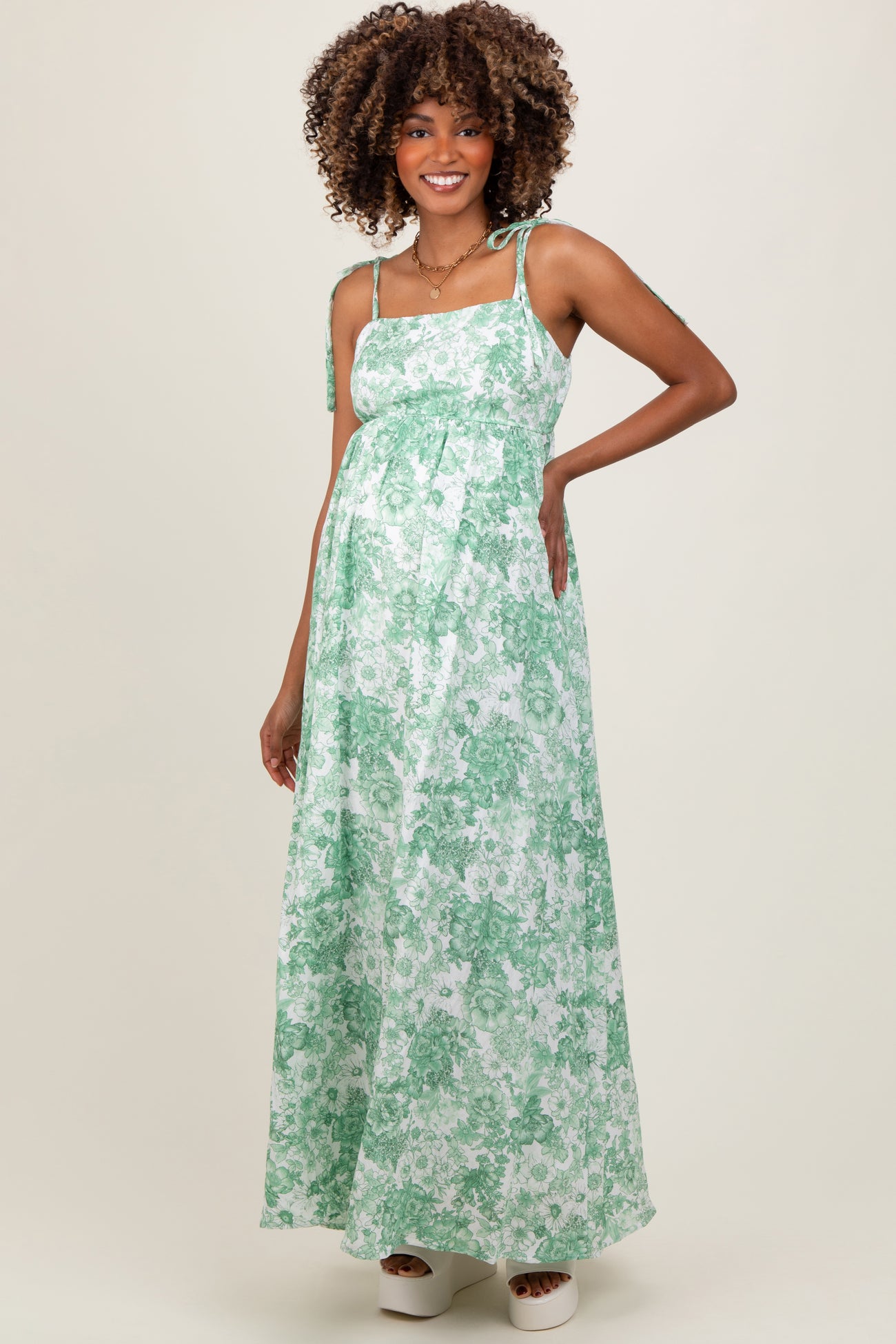 woman wearing a green floral maternity maxi dress with tie straps and a visible baby bump