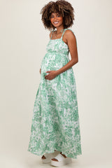 woman wearing a green floral maternity maxi dress, smiling and holding her baby bump