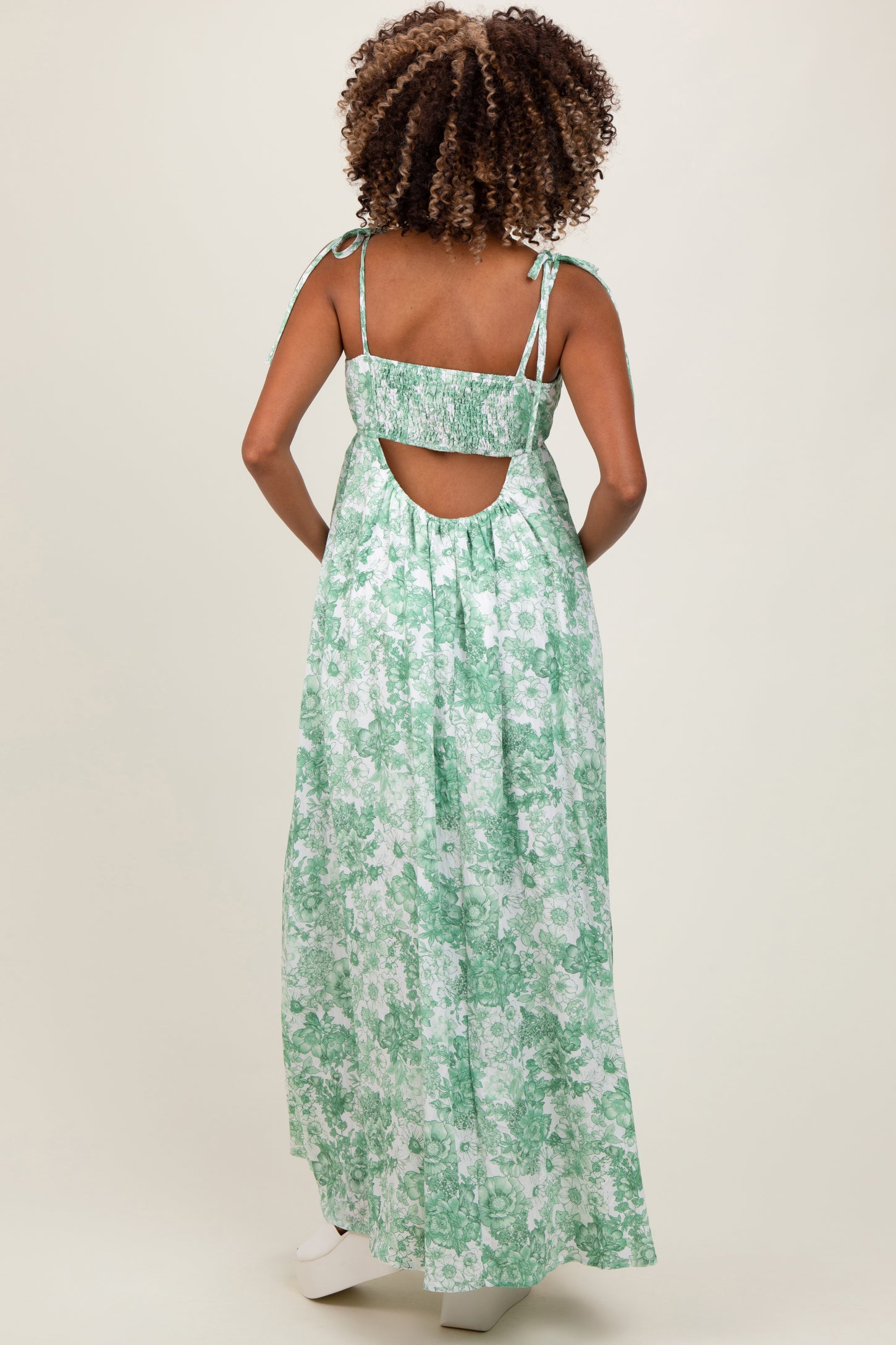 woman wearing a green floral maternity maxi dress with tie straps and an open back, showcasing her baby bump